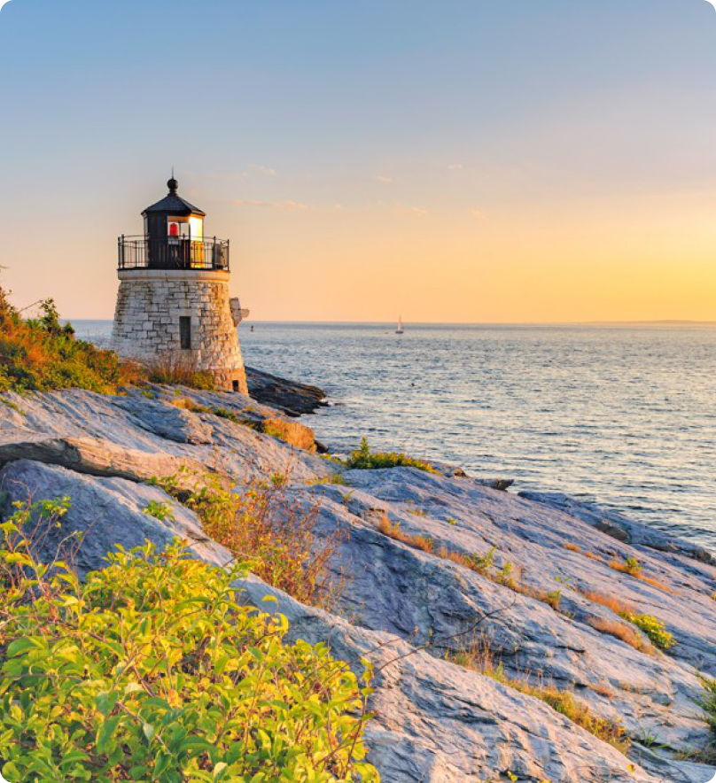 A lighthouse sits along the rocky coast at dusk.