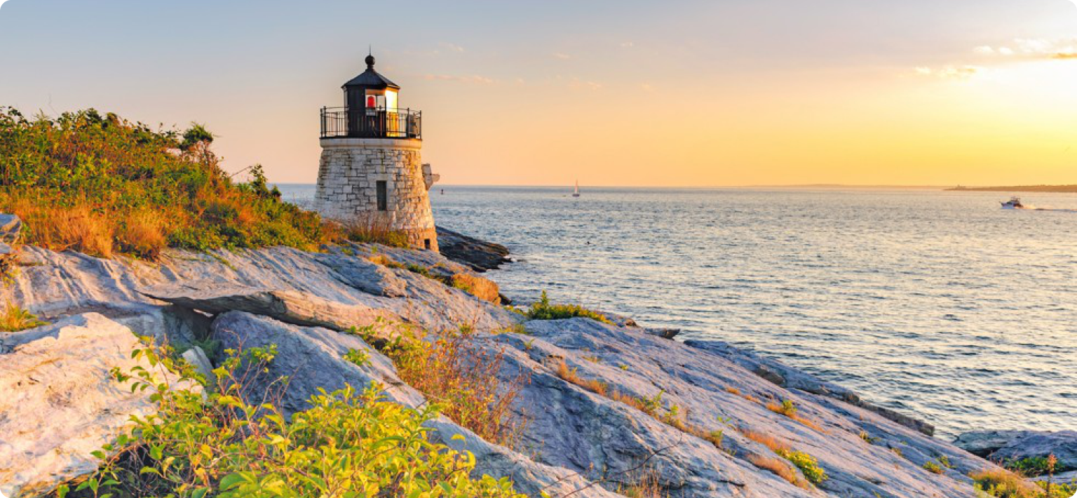 A lighthouse sits along the rocky coast at dusk.