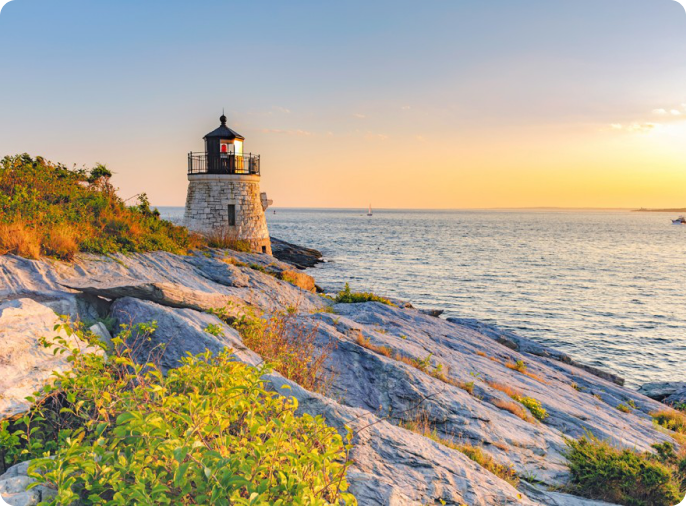 A lighthouse sits along the rocky coast at dusk.